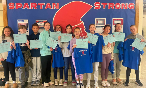 a group of students holding certificates lined up in front of a bulletin board that says "Spartan Strong"