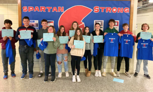 a group of students holding certificates lined up in front of a bulletin board that says "Spartan Strong"